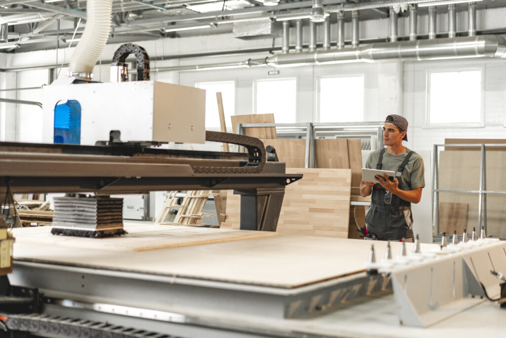 Young carpenter operating machine for wood processing at a furniture factory close up